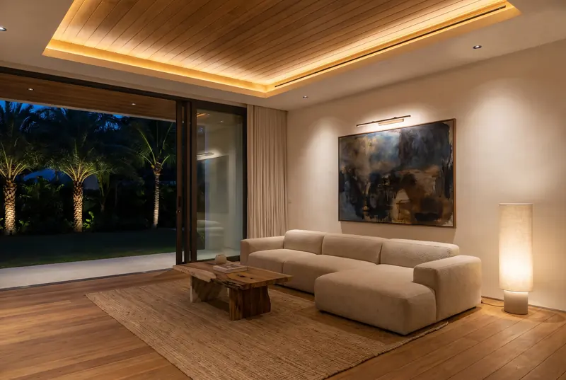 A living room in the evening, lit by a warm ceiling cove, downlights and a picture light.