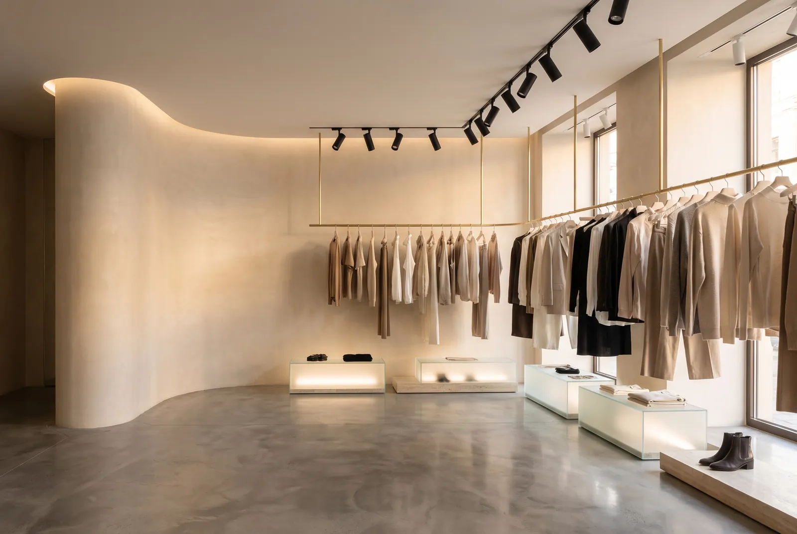 A clothing boutique with black track spotlights over rails of garments, a curved white wall and softly lit display plinths.